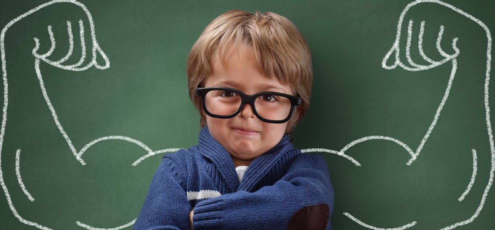 Petit garcon confiant a lunettes, bras croises, muscles dessines a la craie au tableau