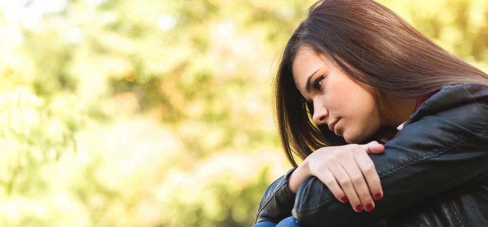 Adolescente pensive en veste de cuir noir, assise dehors, le regard baisse en automne