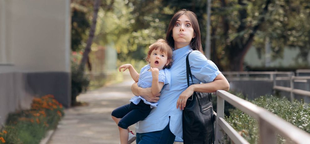 Mère fatiguée portant sa jeune enfant dans les bras dehors, toutes deux en chemise bleue