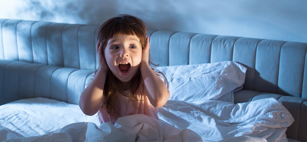 Petite fille terrifiée assise dans son lit la nuit, mains sur les oreilles et bouche ouverte