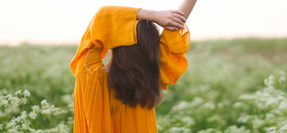 Femme debout dans un champ de fleurs sauvages au coucher du soleil, les yeux fermés, les mains ouvertes en signe de lâcher-prise