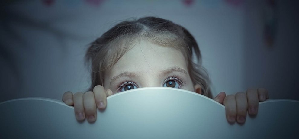 Enfant cachée derrière une tête de lit blanche la nuit, seuls les yeux dépassent